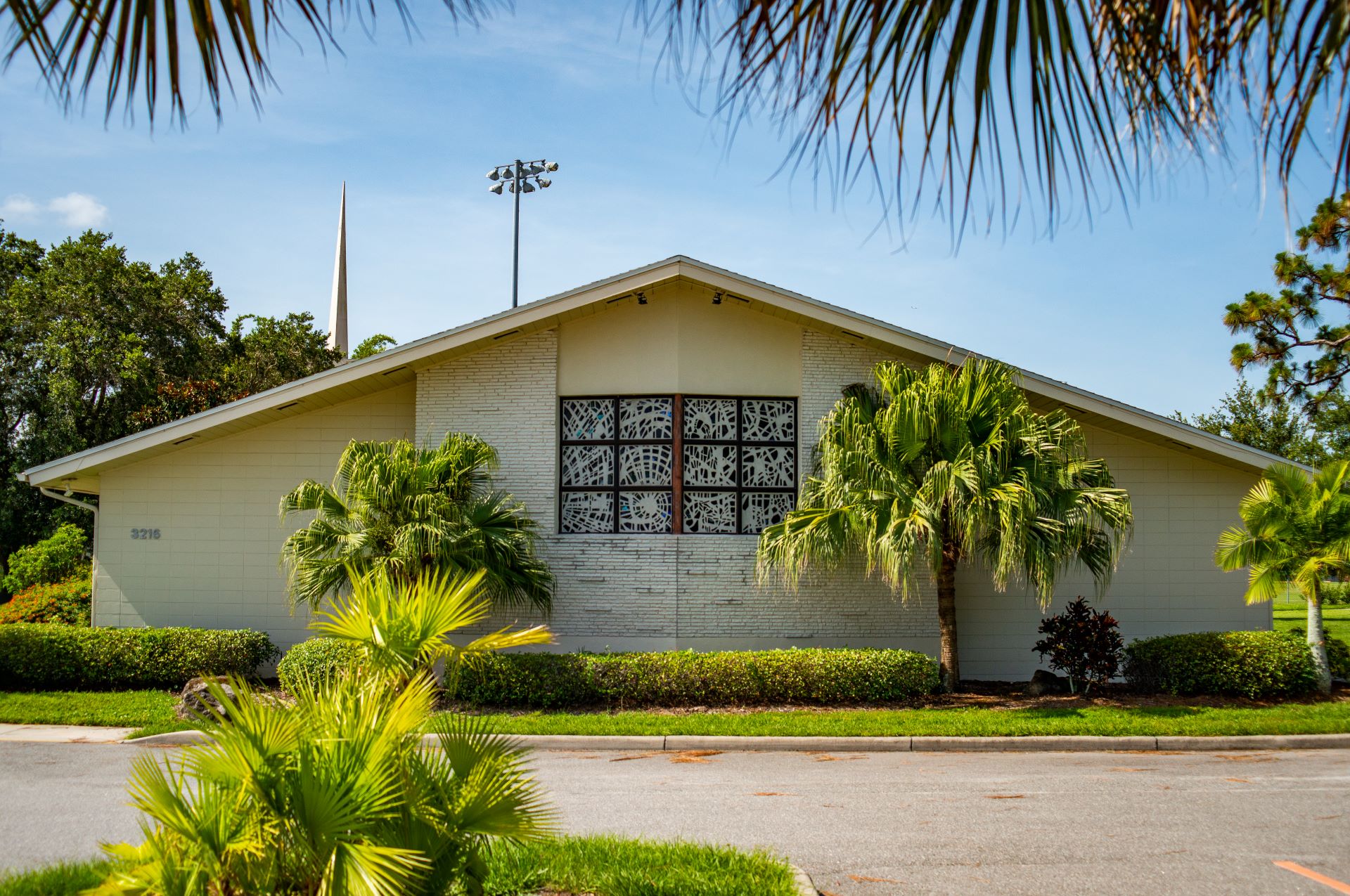Front view of All Faiths Center at Florida Tech, showcasing the decorative windows and the surrounding palm trees and bushes