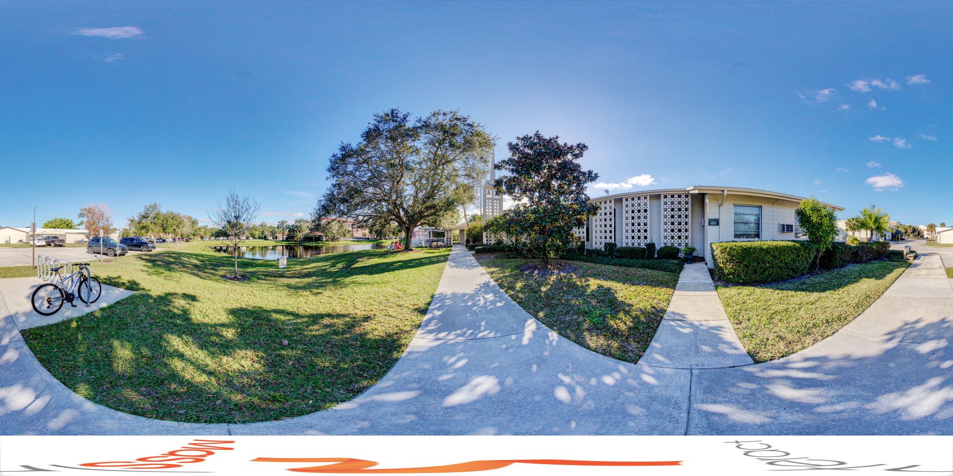 Outside view of All Faiths Center at Florida Tech, showing a path leading to the building with a pond and bike rack in the foreground