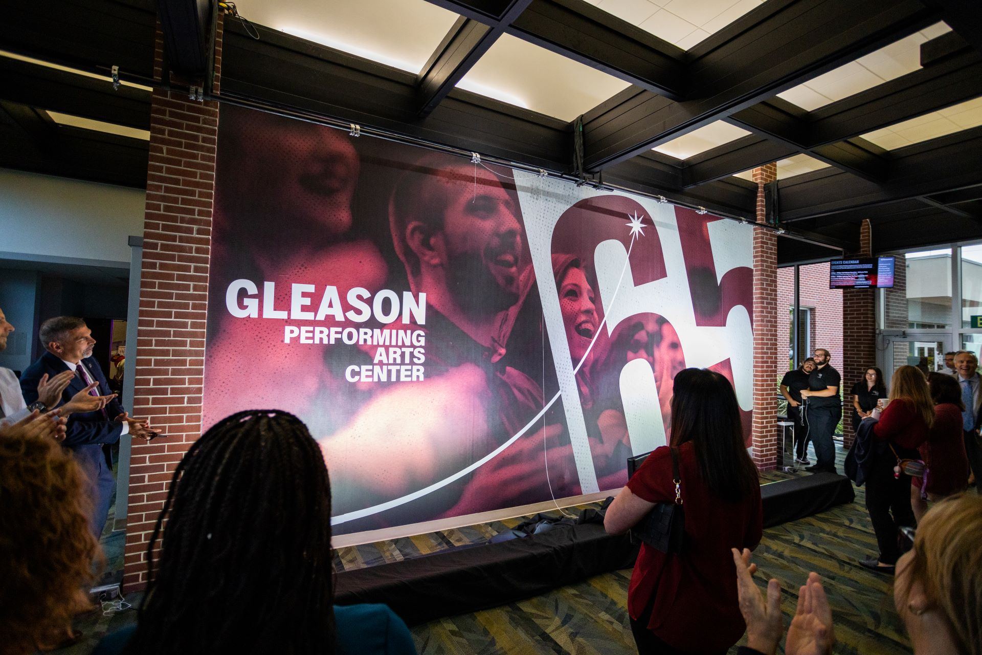 People gather in the lobby of the Gleason Performing Arts Center at Florida Tech, where a large, colorful sign prominently displays the center's name