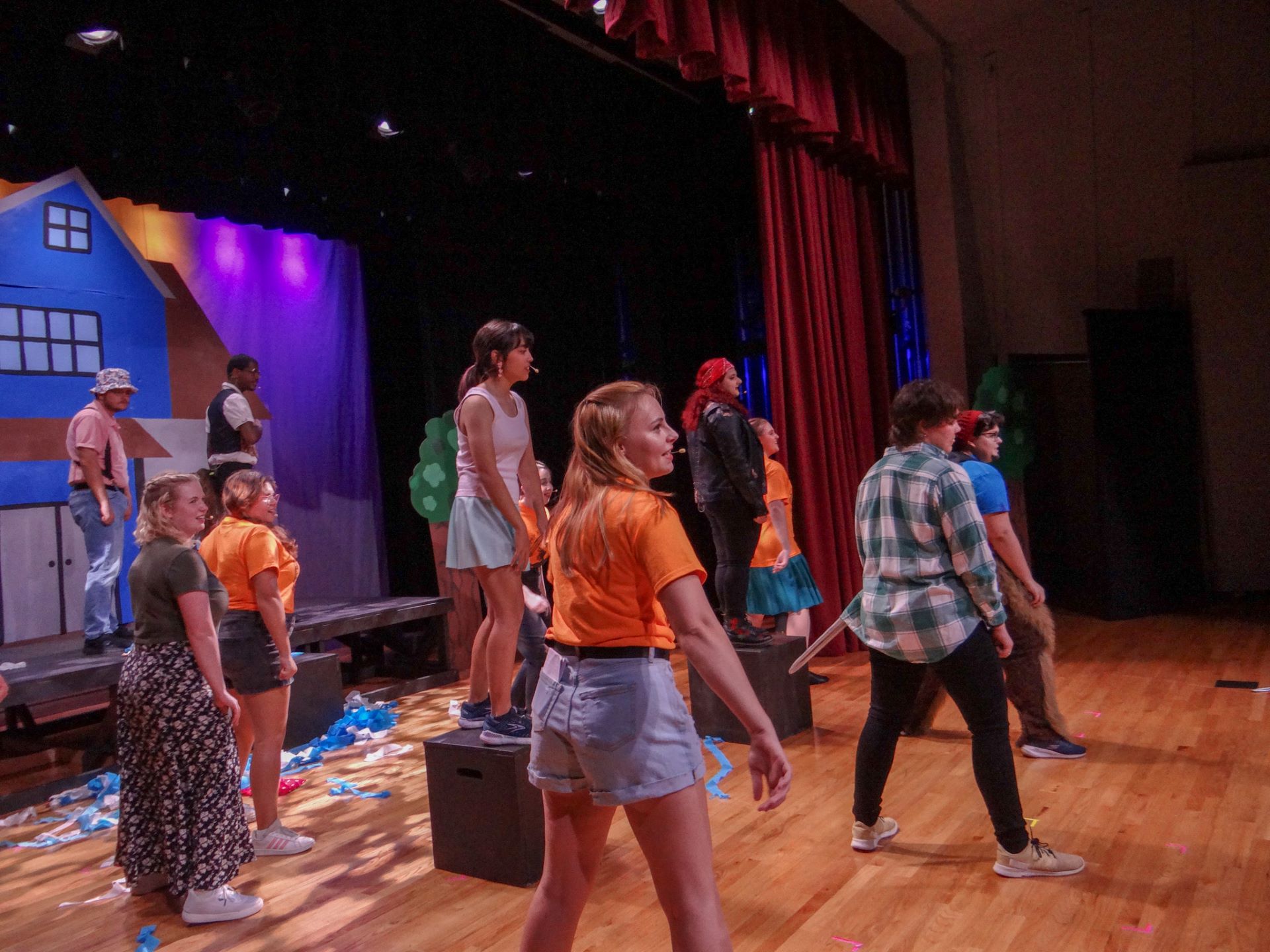 Students performing a lively scene on stage at the Gleason Performing Arts Center, with vibrant lighting and a colorful set