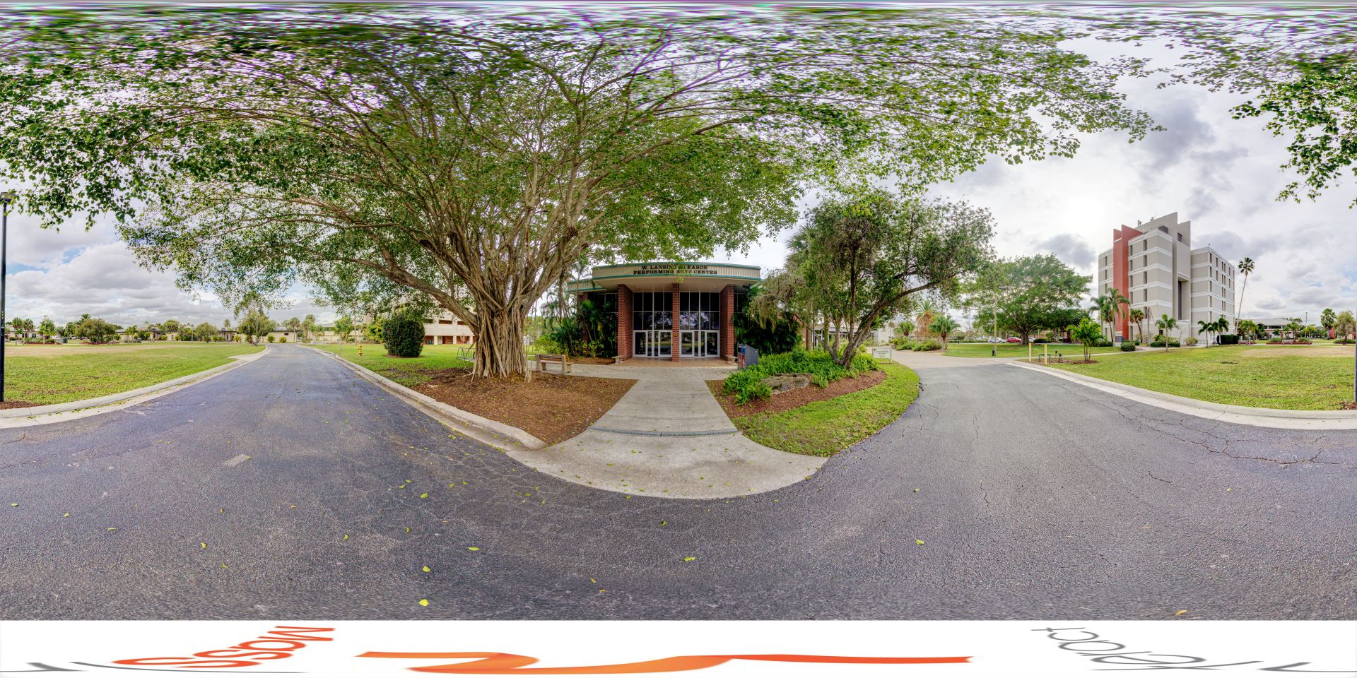 Panoramic view of the Gleason Performing Arts Center at Florida Tech, showcasing the building surrounded by lush trees and greenery, with a clear path leading to its entrance