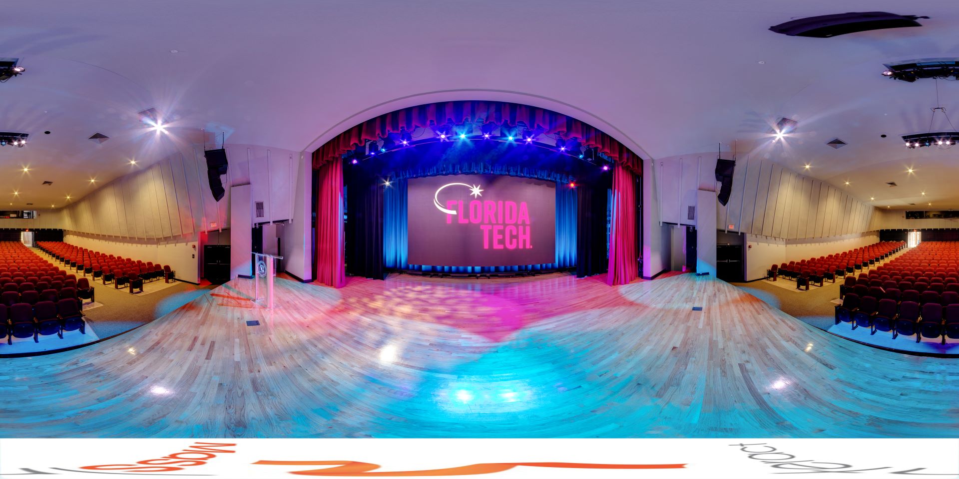 Wide-angle view of the Gleason Performing Arts Center auditorium, showcasing the stage, seating area, and vibrant lighting setup, with the Florida Tech logo displayed prominently on the screen