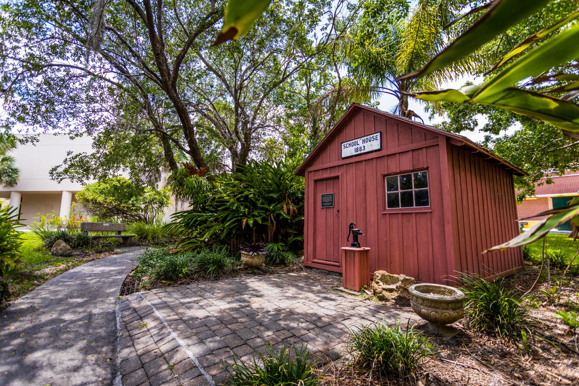 A small, historical schoolhouse from 1883 surrounded by lush greenery and a winding path in the Botanical Garden at Florida Tech