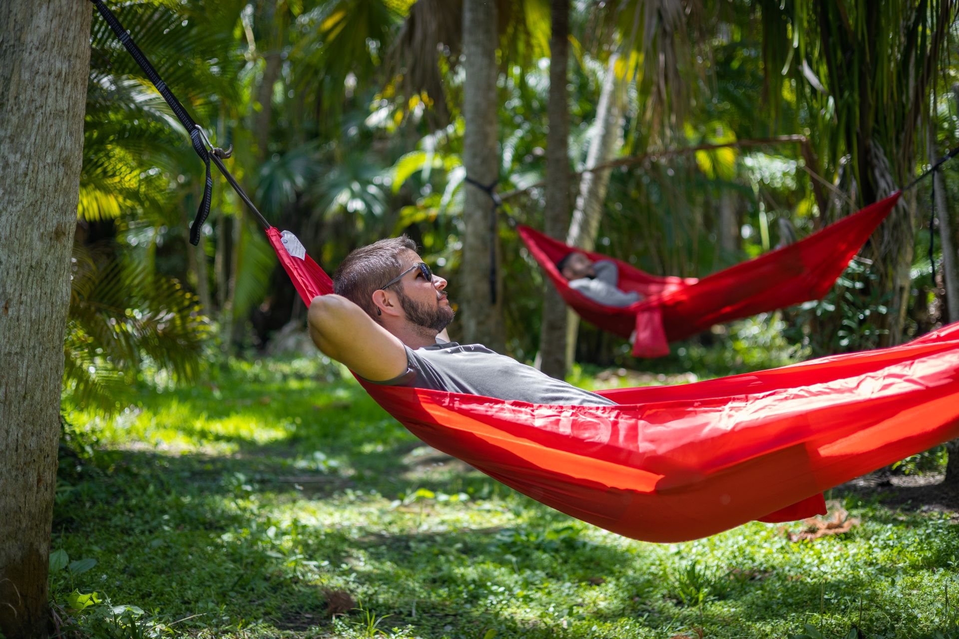 Two people relaxing in red hammocks amidst the tropical greenery of the Joy and Gordon Patterson Botanical Garden at Florida Tech