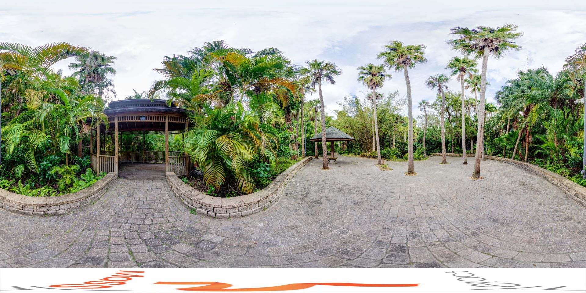 Panoramic view of a serene area within the Joy and Gordon Patterson Botanical Garden at Florida Tech, featuring a wooden gazebo surrounded by lush tropical greenery and tall palm trees