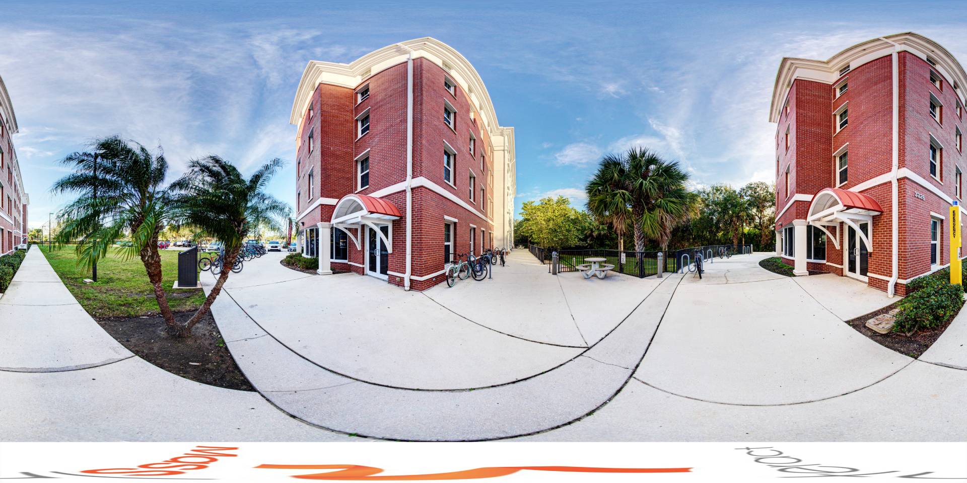 Panoramic view of a red brick dormitory with palm trees and bicycles leaning against the building.