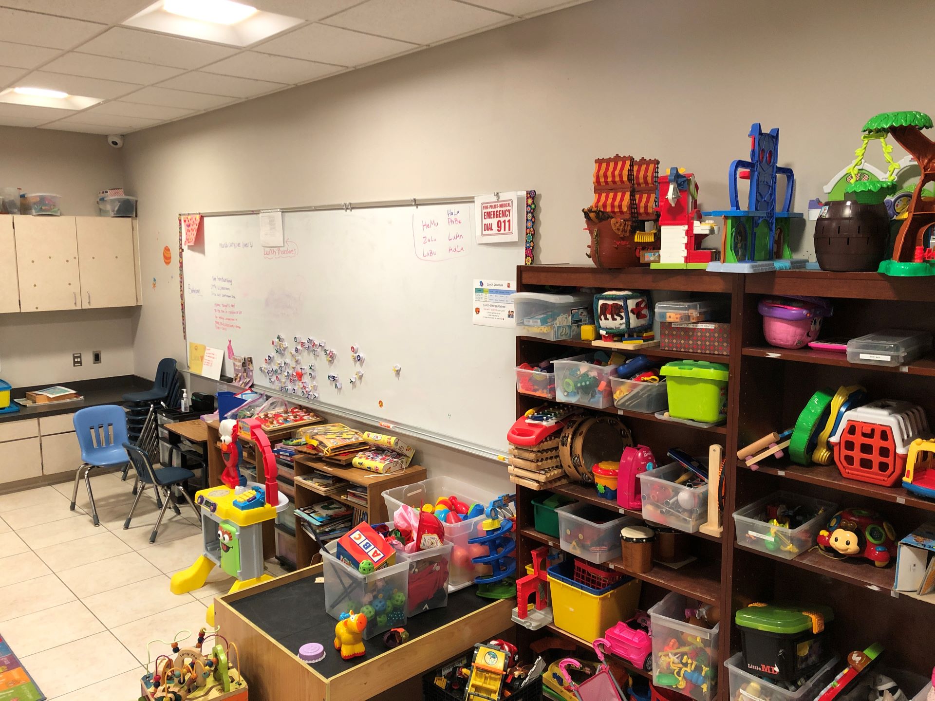 A playroom with shelves full of toys and a whiteboard with something written on it, along with magnetic letters attached