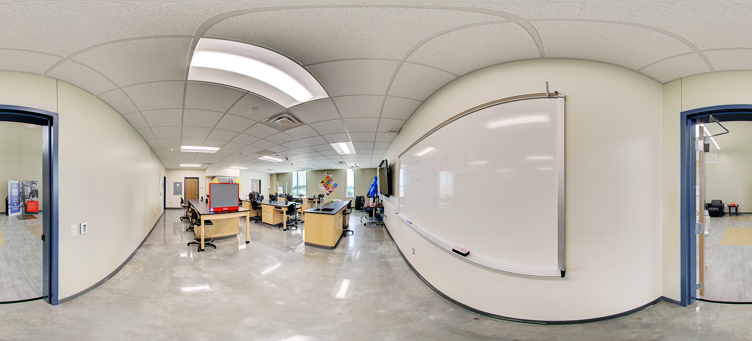 Panoramic view of a classroom lab with polished floors, featuring workstations with equipment and stools, a large whiteboard on the wall, and adjacent rooms visible through open doorways under bright ceiling lights.