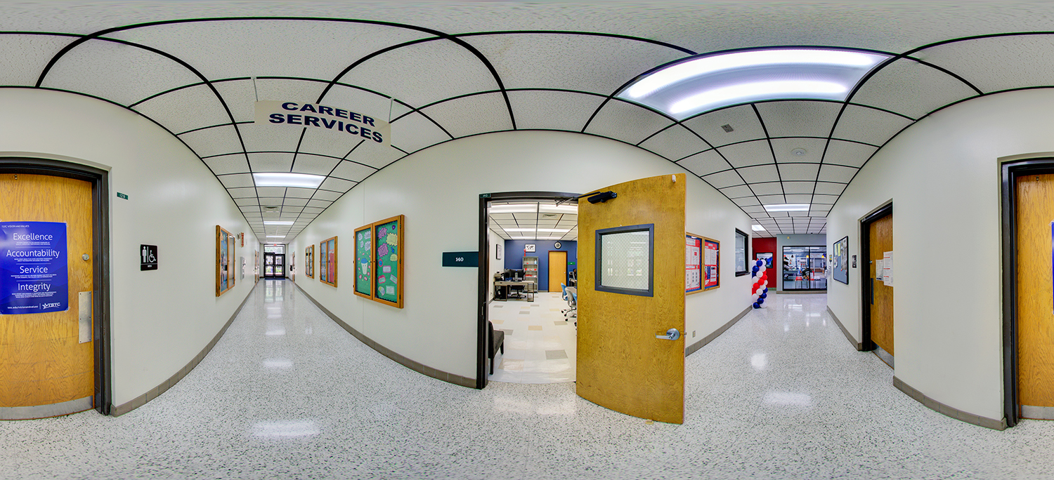 Panoramic view of a clean institutional hallway with “Career Services” signage overhead, bulletin boards along the walls, and an open office door revealing a workspace inside, all under bright fluorescent ceiling lights.