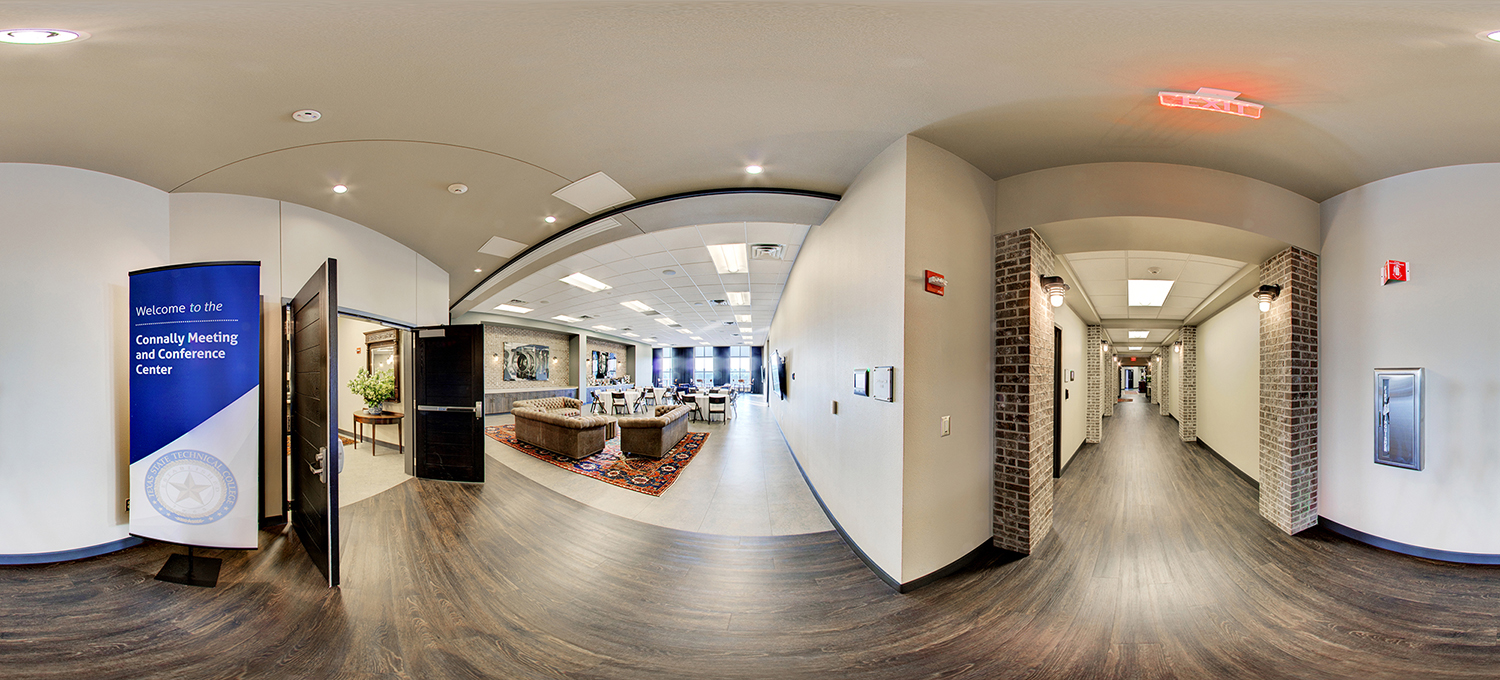Panoramic view of the entrance to a conference center, featuring a sign reading “Connally Meeting and Conference Center,” an open doorway leading to a lounge with sofas and tables, and a hallway with brick accents extending to the right.