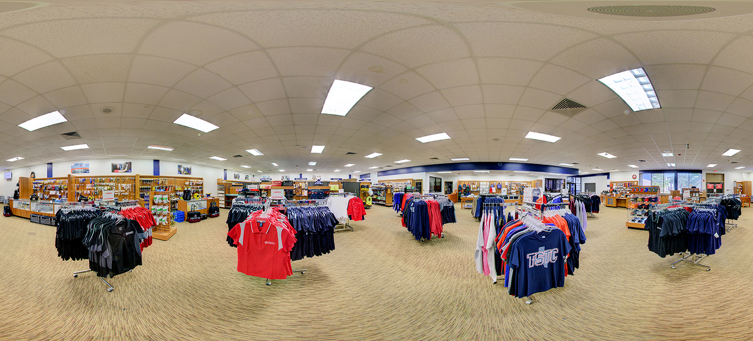 Panoramic view of a campus bookstore filled with racks of TSTC-branded clothing, including shirts and jackets, along with shelves of accessories and supplies under bright overhead lighting.