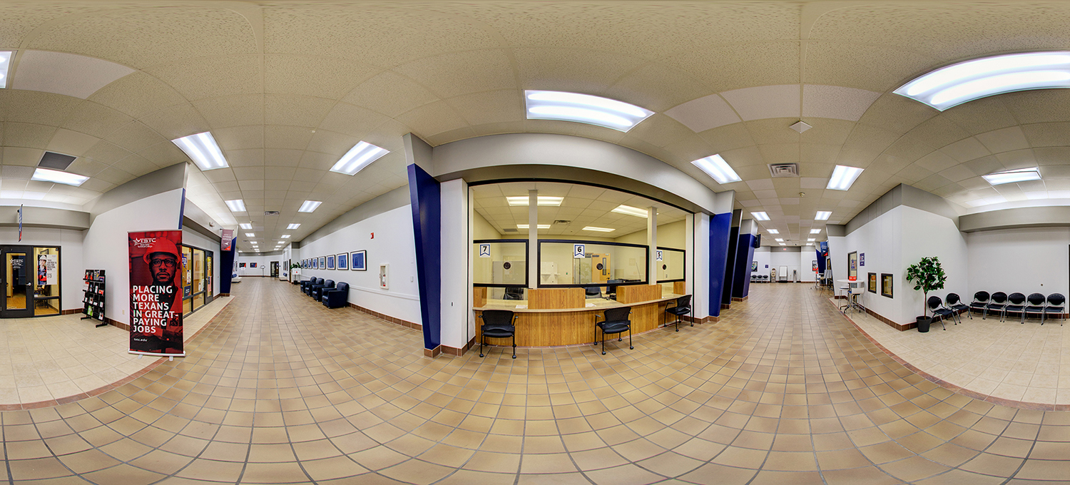 Panoramic view of a campus administrative lobby with a central service counter behind glass windows, tiled floors, rows of waiting chairs along the walls, and informational posters and signage throughout.