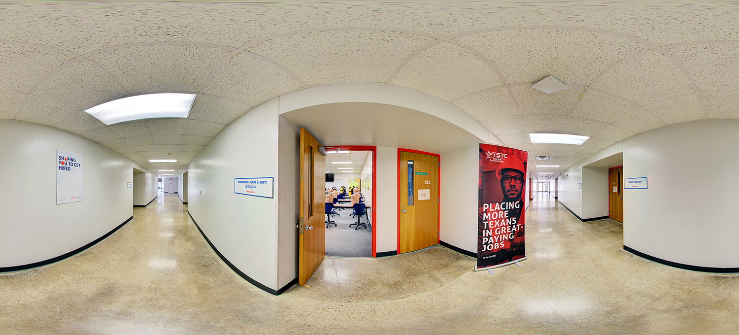 Panoramic view of an indoor hallway in an academic building, with open classroom doors revealing students seated inside, informational posters on the walls, and a banner promoting job placement standing along the corridor.