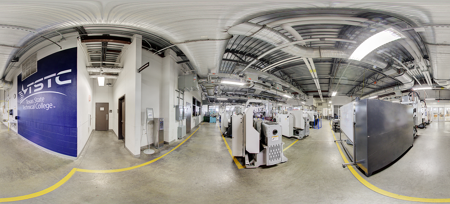 Panoramic view of an advanced manufacturing lab at Texas State Technical College, featuring rows of industrial machines, CNC equipment, and control units beneath exposed ductwork, with clearly marked walkways and utility stations along the walls.