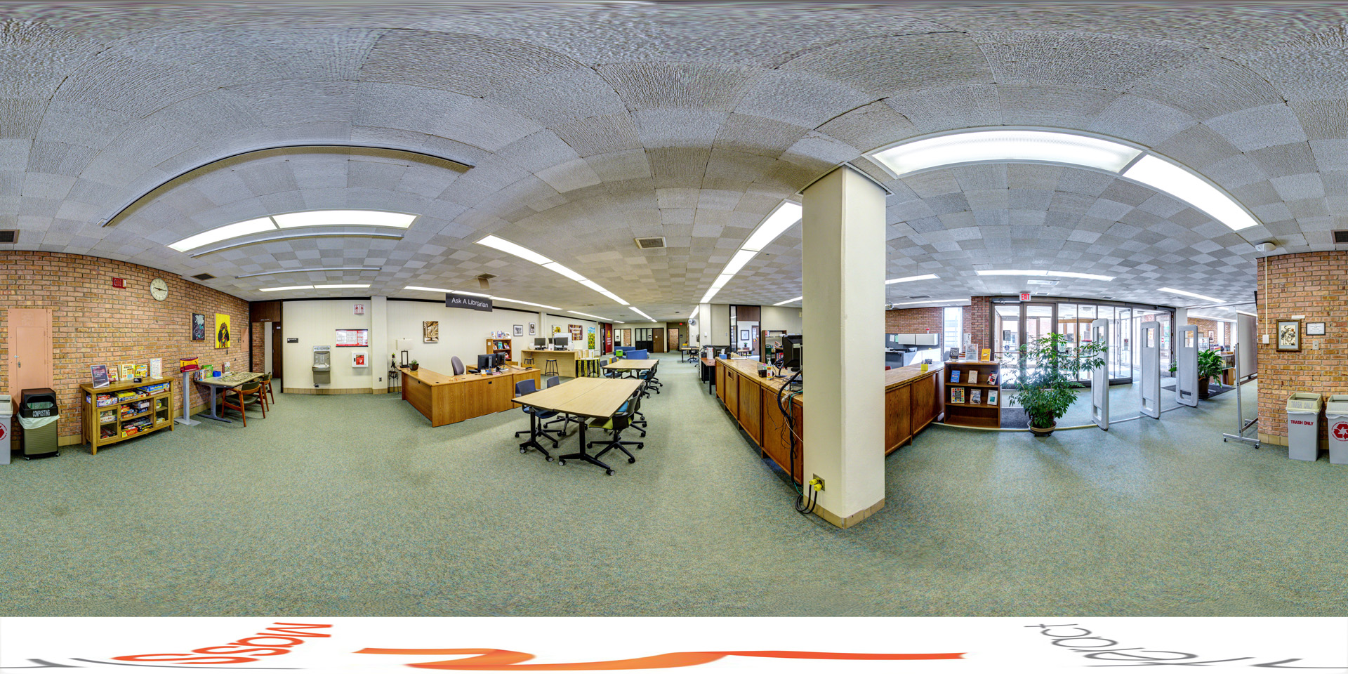 Panoramic view of a spacious student success center with multiple tables and chairs for group work, a help desk labeled 'Ask A Librarian,' and several bookshelves. The room has brick walls, a checkered ceiling with bright fluorescent lighting, and large windows near the entrance allowing natural light to enter.