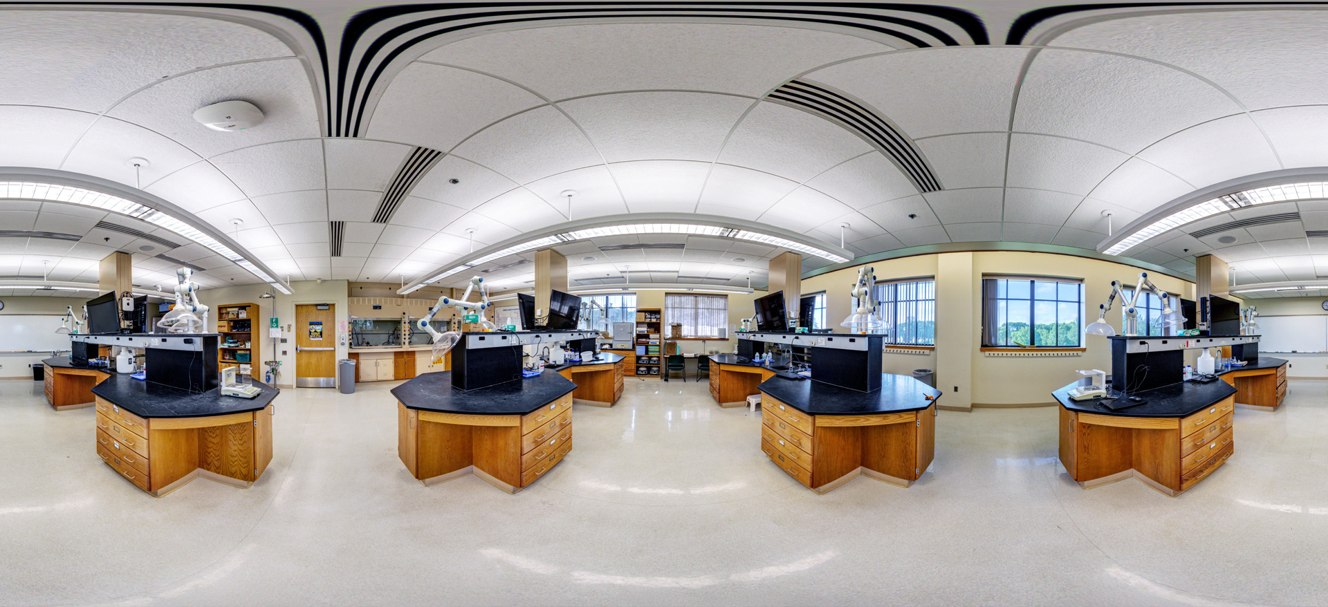 360-degree view of a modern science laboratory with multiple workstation islands, microscopes and lab equipment, large windows, and bright overhead lighting.