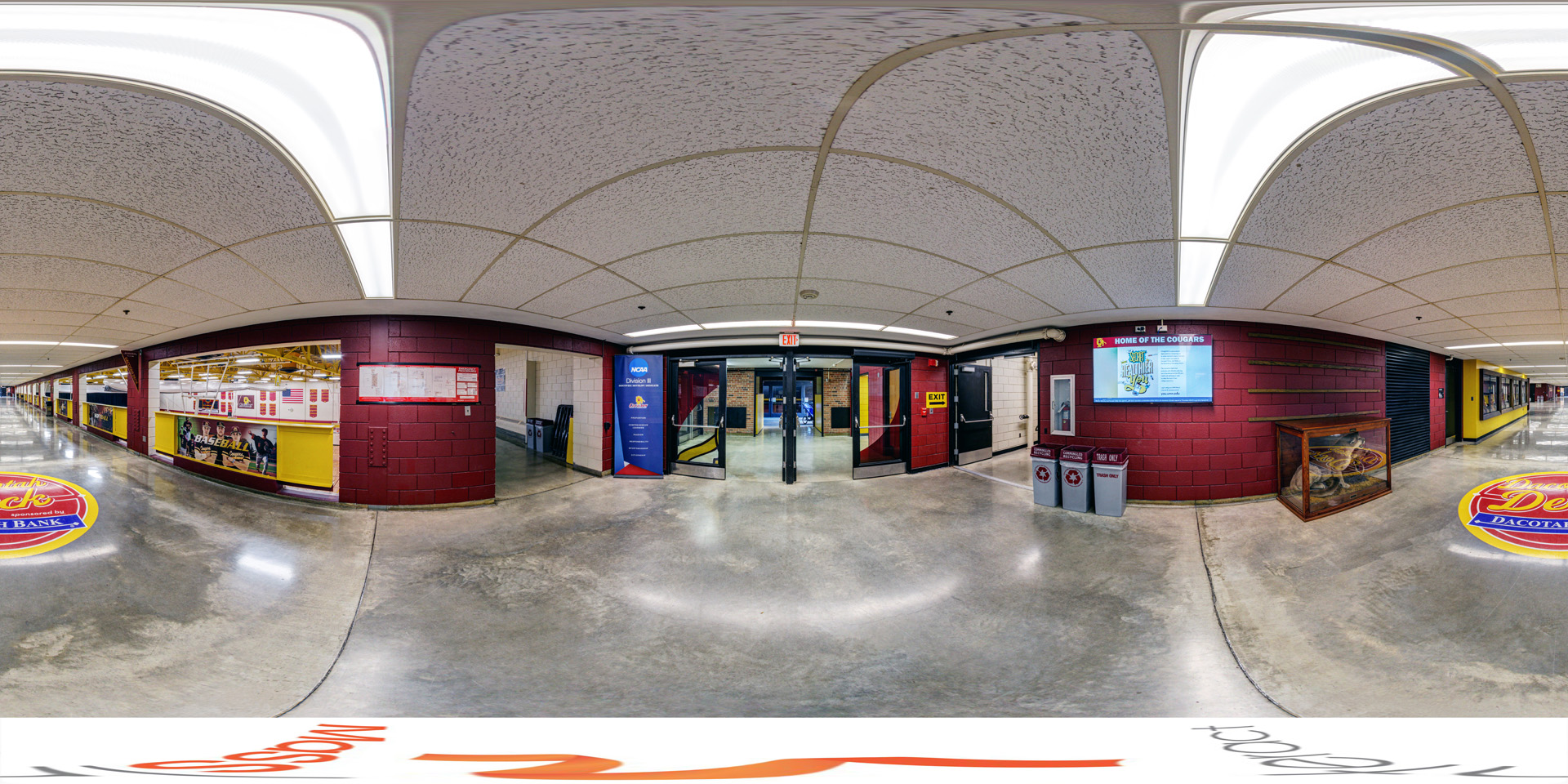Panoramic view of the entrance to the Dacotah Deck in the Cougar Sports Center, with wide hallways, a display case, and sports banners. 