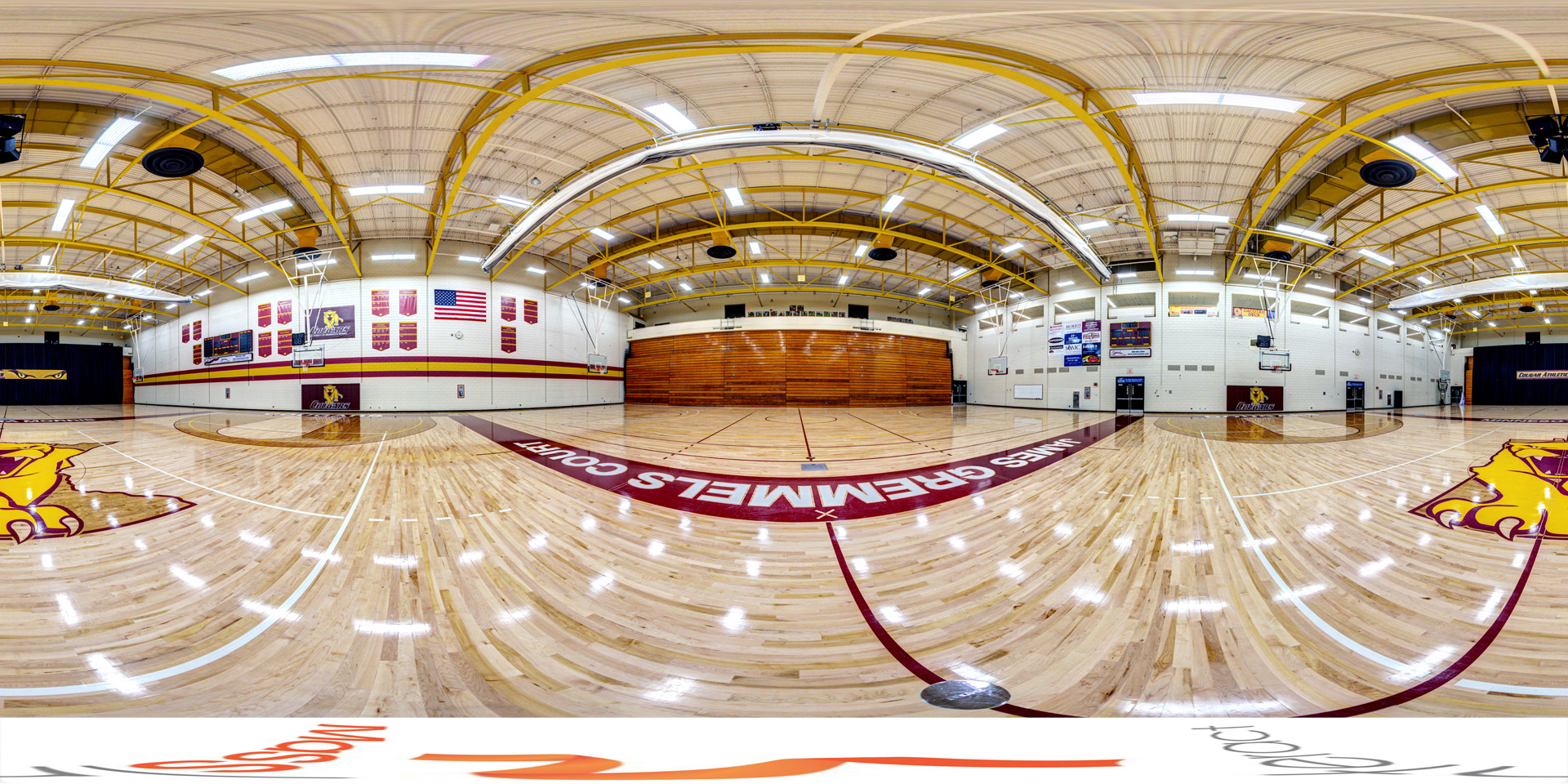 Panoramic view of a wide view of the gymnasium featuring polished hardwood floors, basketball hoops, banners, and bleachers at the back.
