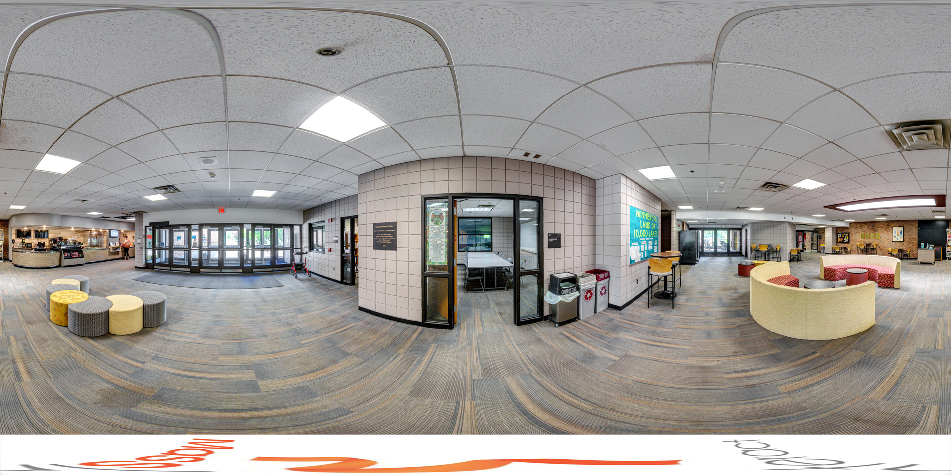 Panoramic view of a spacious lobby with modern seating, a cafe counter to the left, and a meeting room enclosed by glass walls inside the Regional Fitness Center.