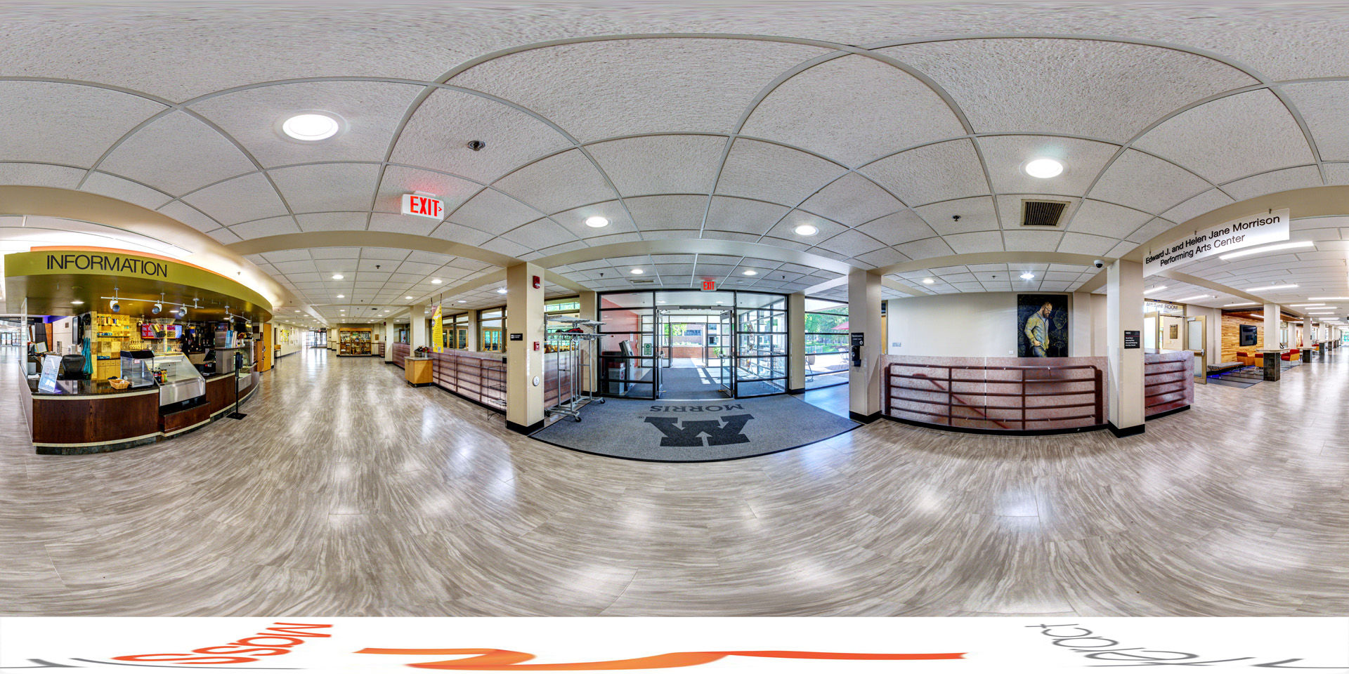 Panoramic view of the entrance area of a building featuring a coffee shop labeled 'Information' to the left, wide glass doors in the center with a large 'Morris' logo on the floor mat, and hallways leading to different sections, including the Edward J. and Helen Jane Morrison Performing Arts Center. 