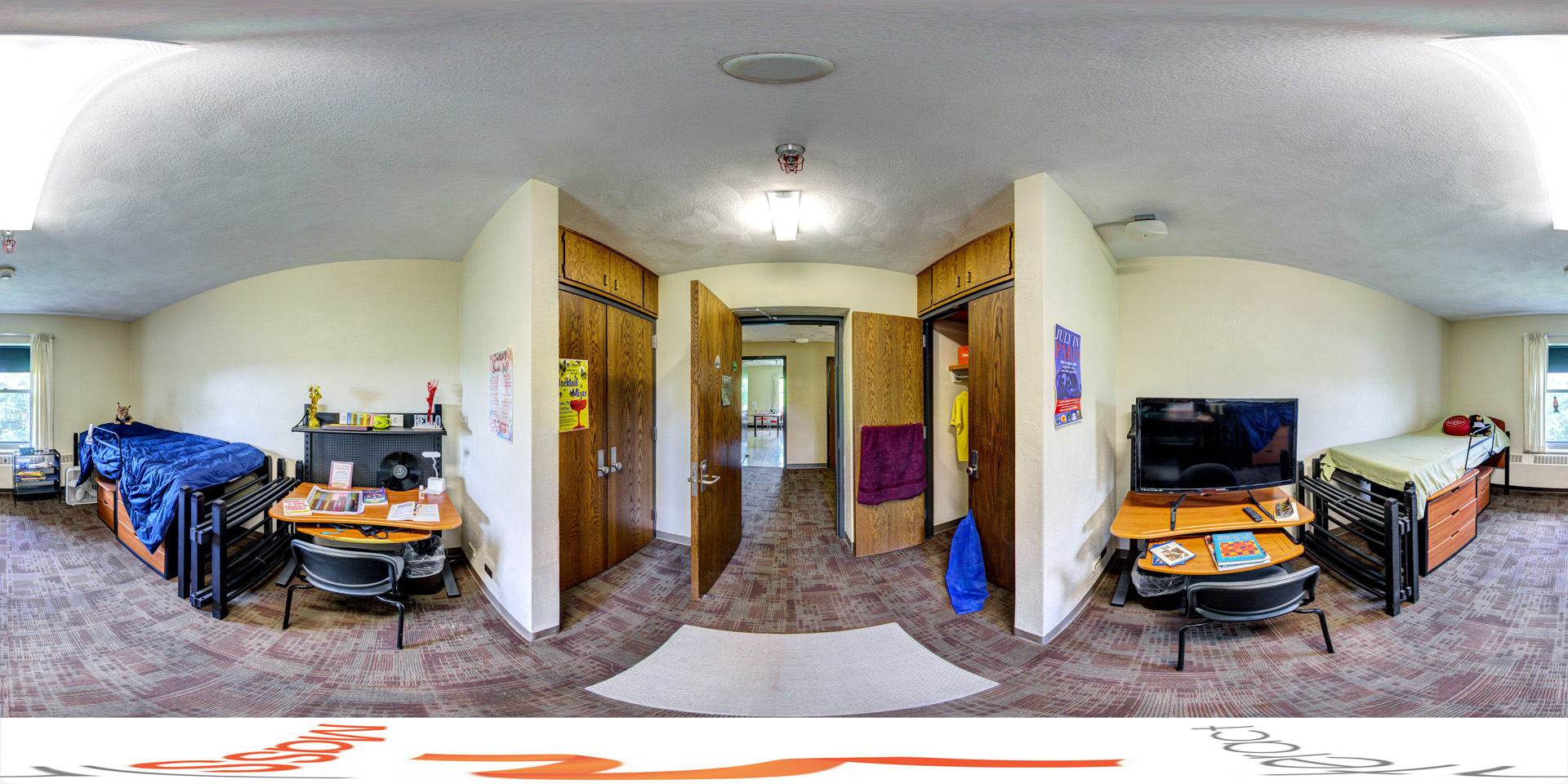 Panoramic view of a shared dorm room with two single beds placed on either side of the room, both with raised bed frames and storage drawers underneath. Each side of the room features a desk with various study materials and a TV on one side. The center of the room leads to an open doorway with closets on both sides.